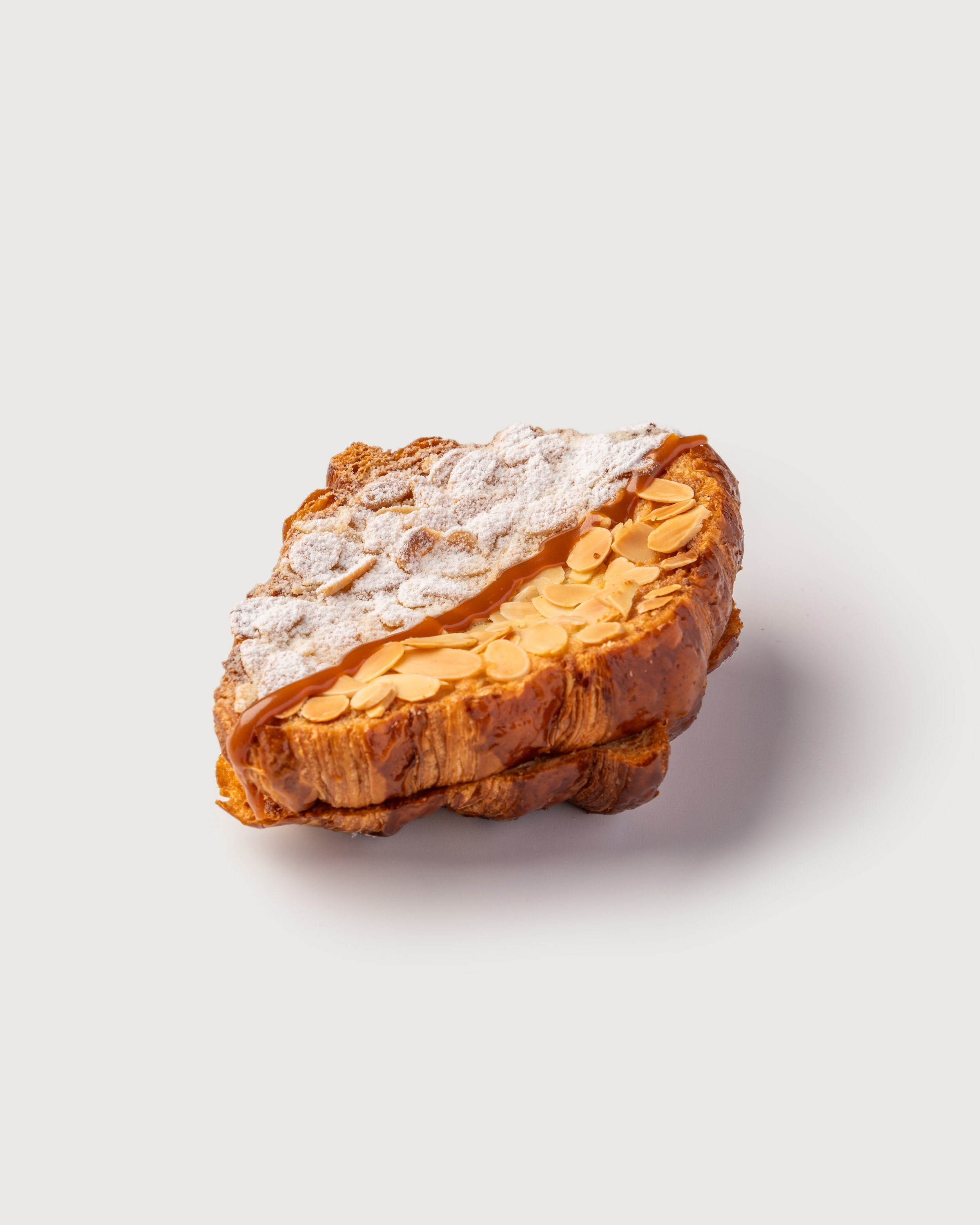 Close-up of almond croissant topped with powdered sugar and caramel, against a white background.