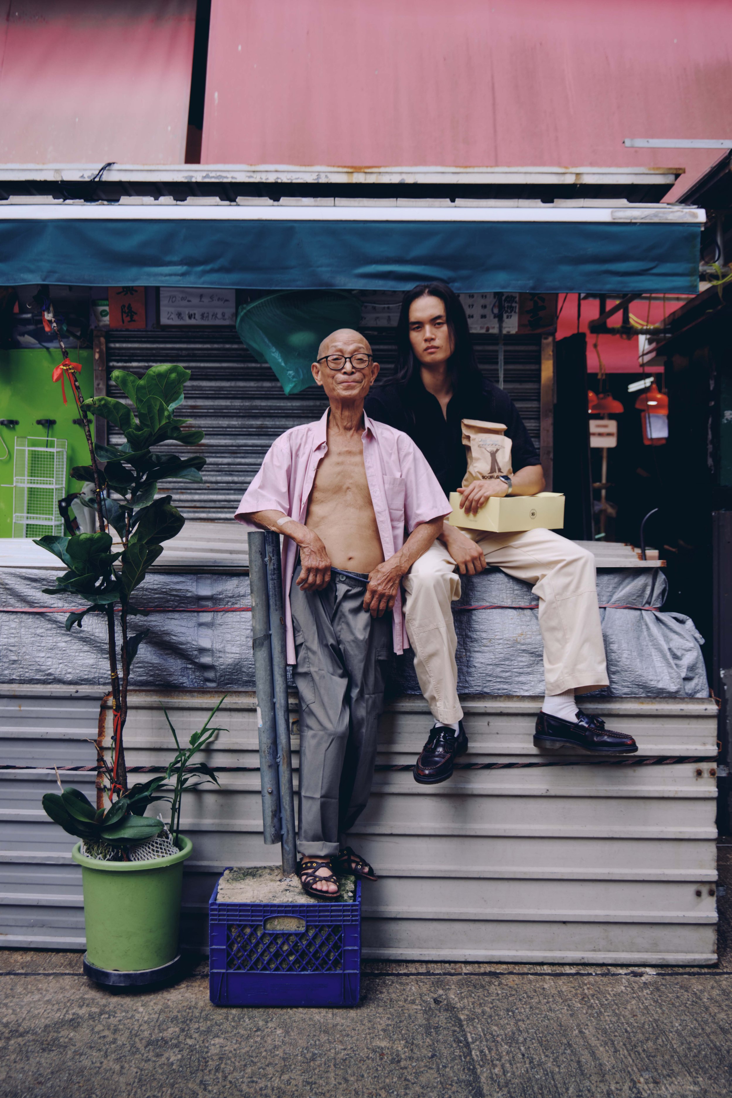 An elderly local resident and a young woman sit together outside a shuttered Hong Kong storefront, evoking the neighbourhood's old-world charm. (Modern Nostalgia)