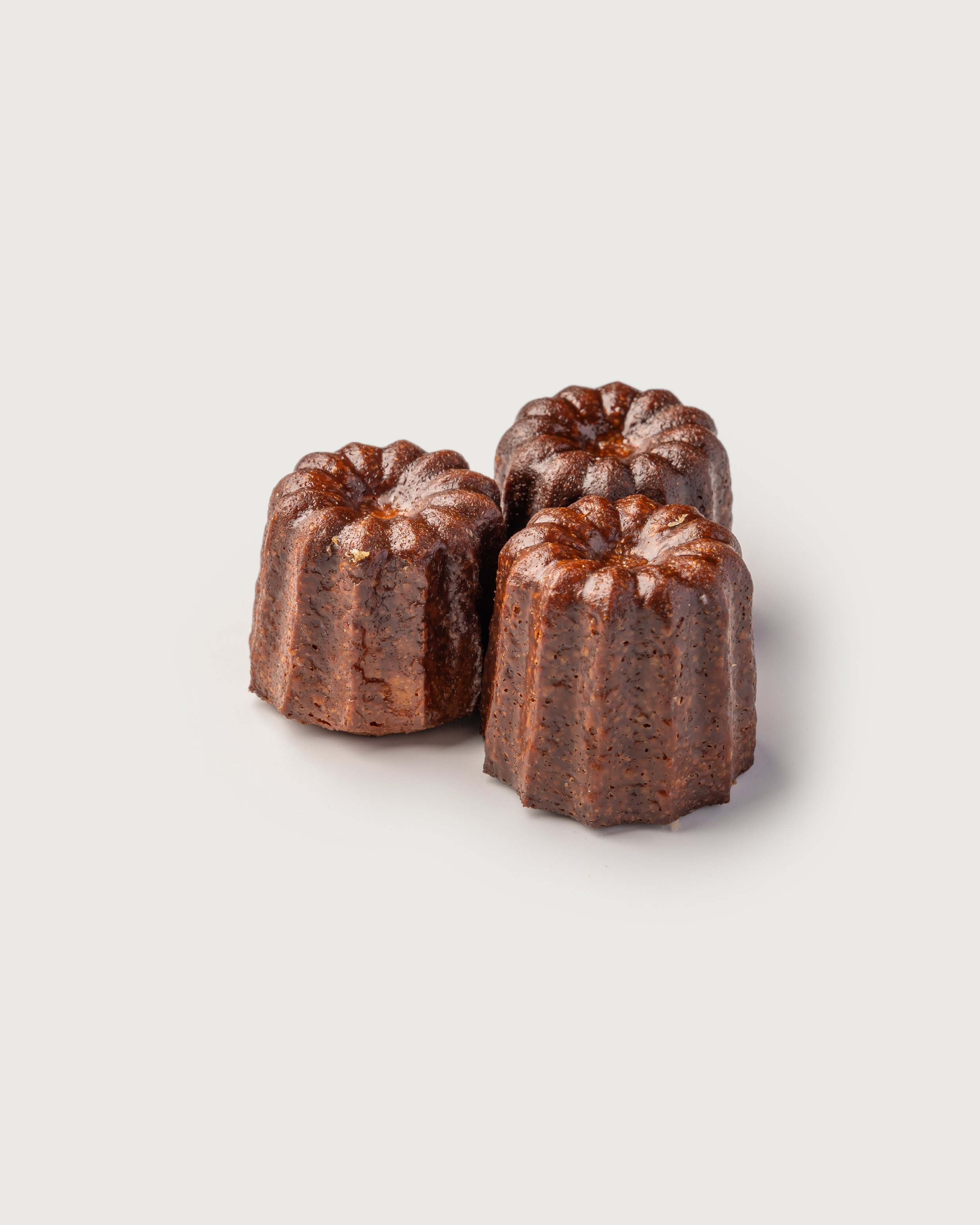 Three cooked cannelés, small French pastries with caramelized crust and soft interior.