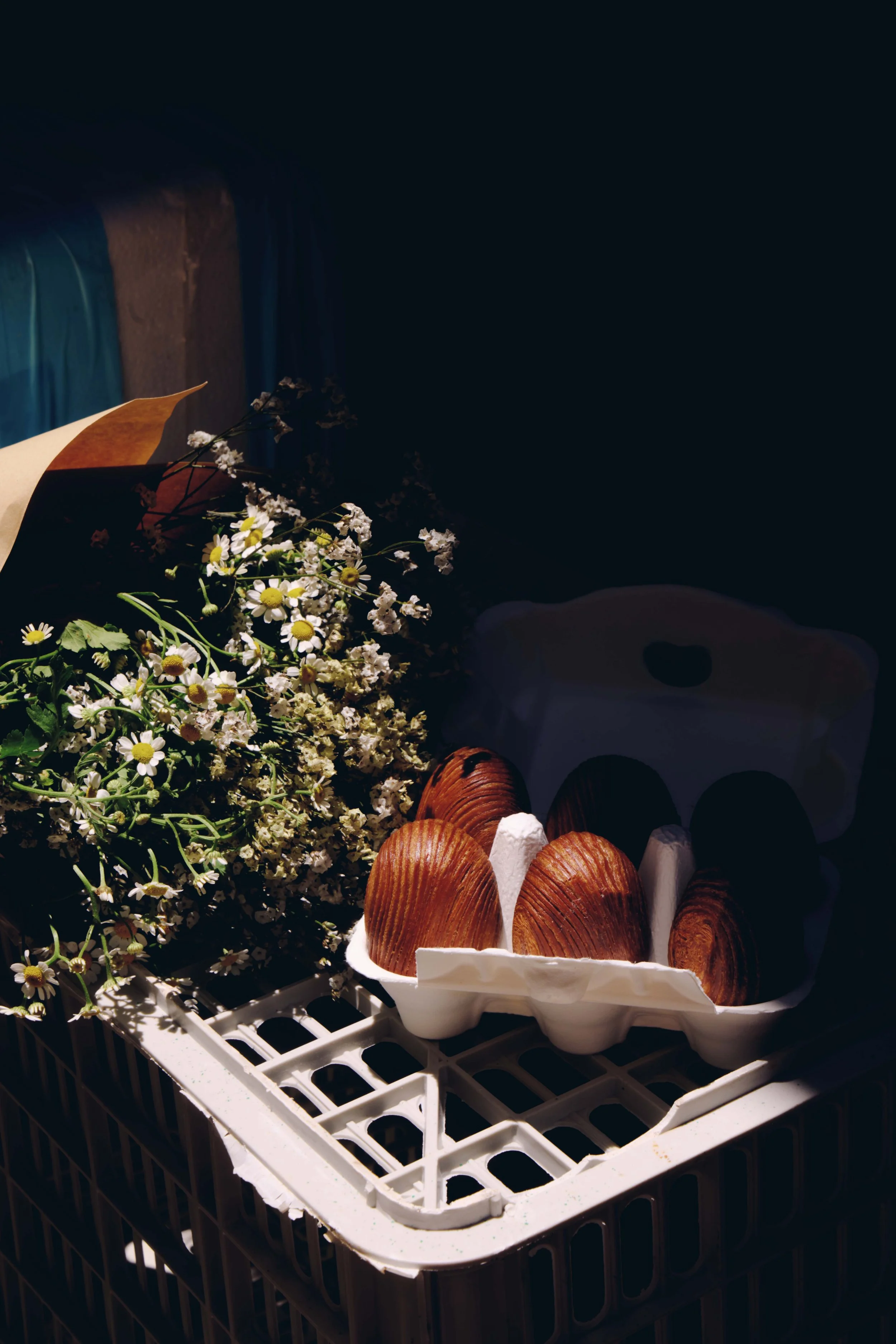 A styled tray of pastries and pink muffins alongside a bouquet of daisies and dried flowers, shot in moody dark tones.