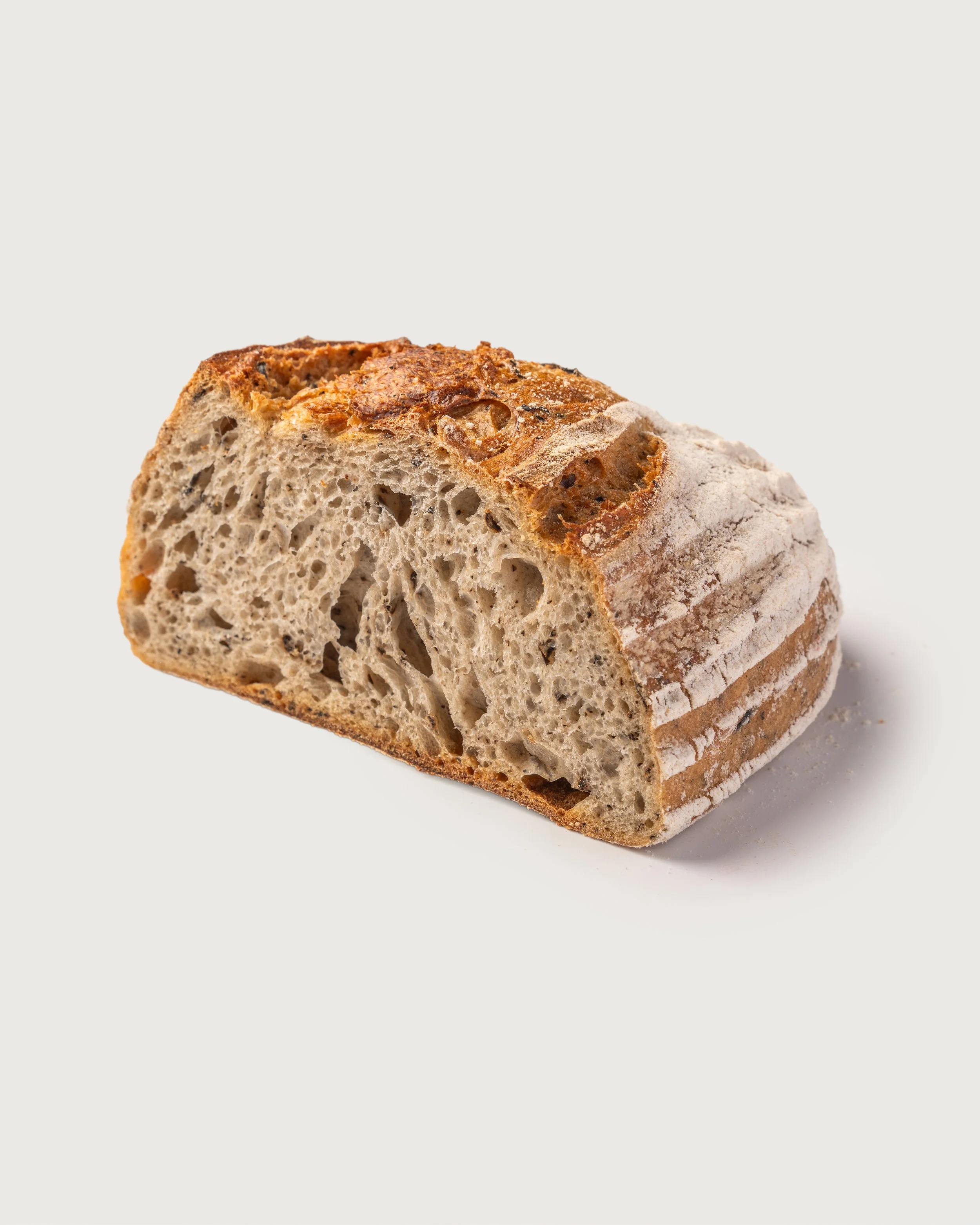 A close-up of a slice of rustic bread with a crispy crust and airy crumb, on a plain light background.