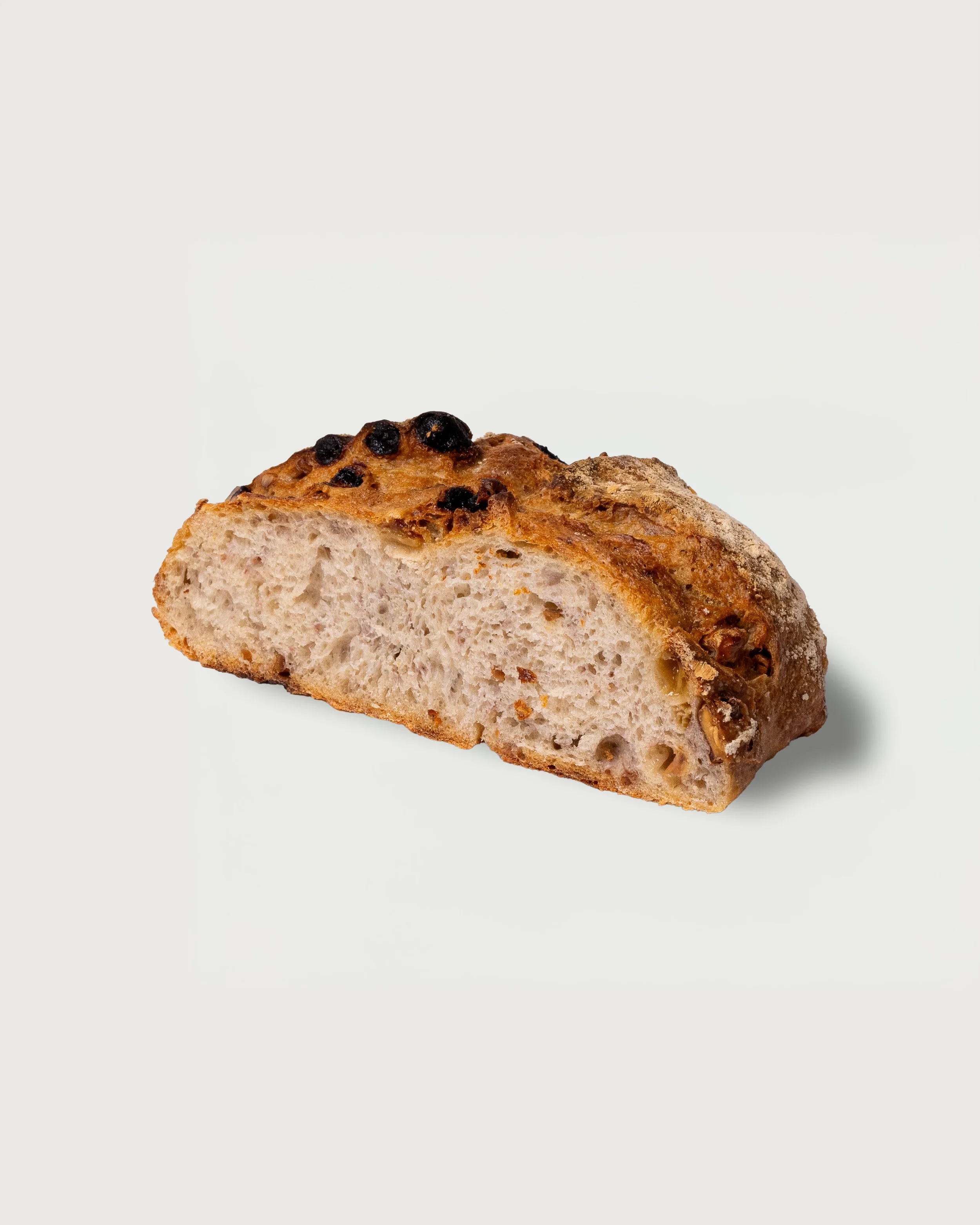 A slice of artisanal bread with a golden crust, topped with blueberries, on a white background.