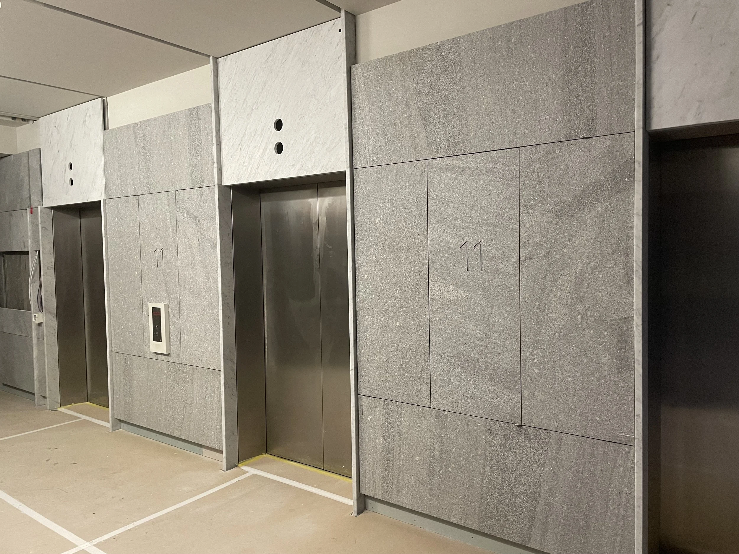 Three elevators with gray stone walls surrounding them in a parking garage or basement area.