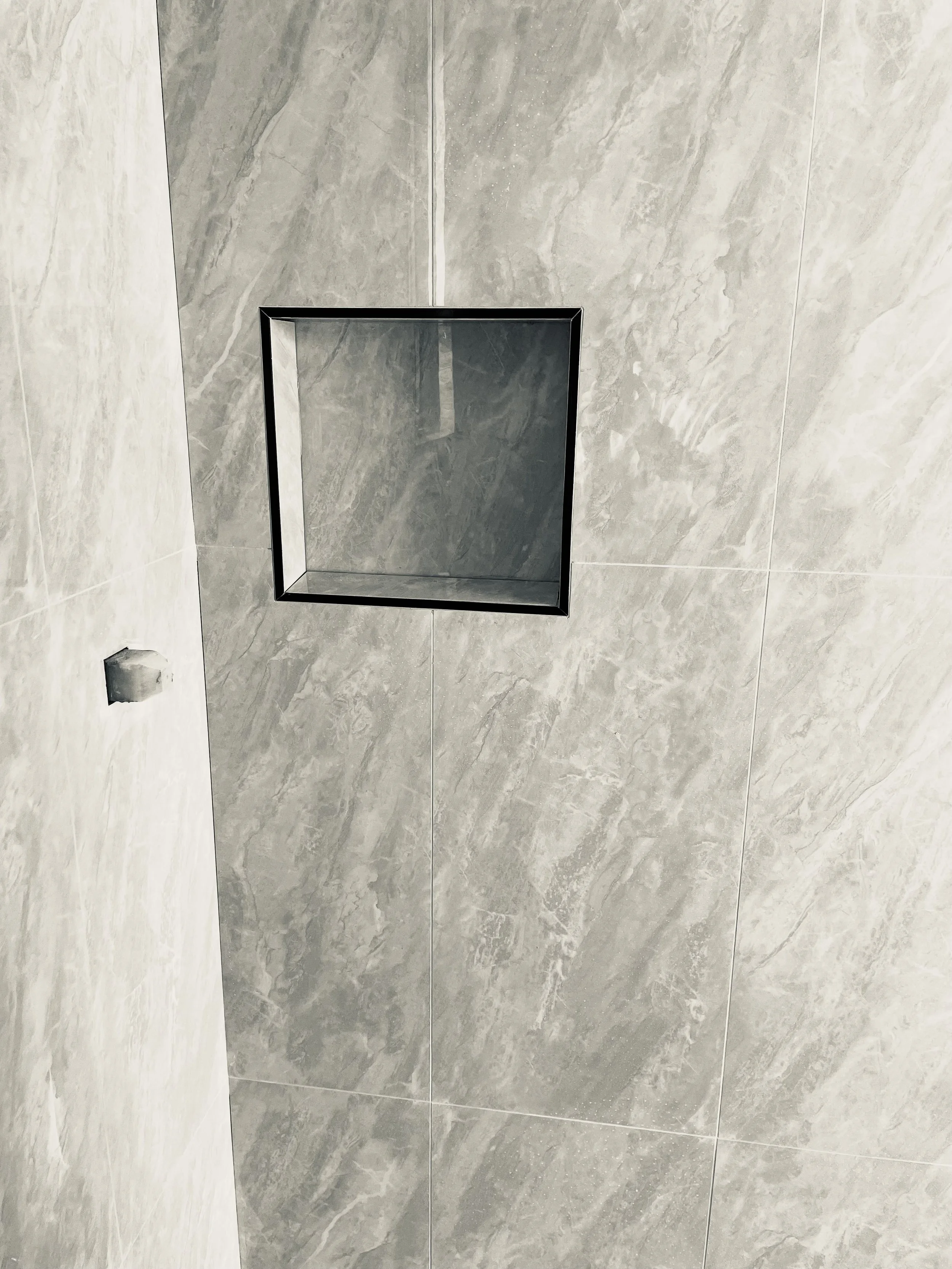 Close-up view of a gray tiled ceiling with a square recessed lighting fixture and a small hole in the tiles to the left.