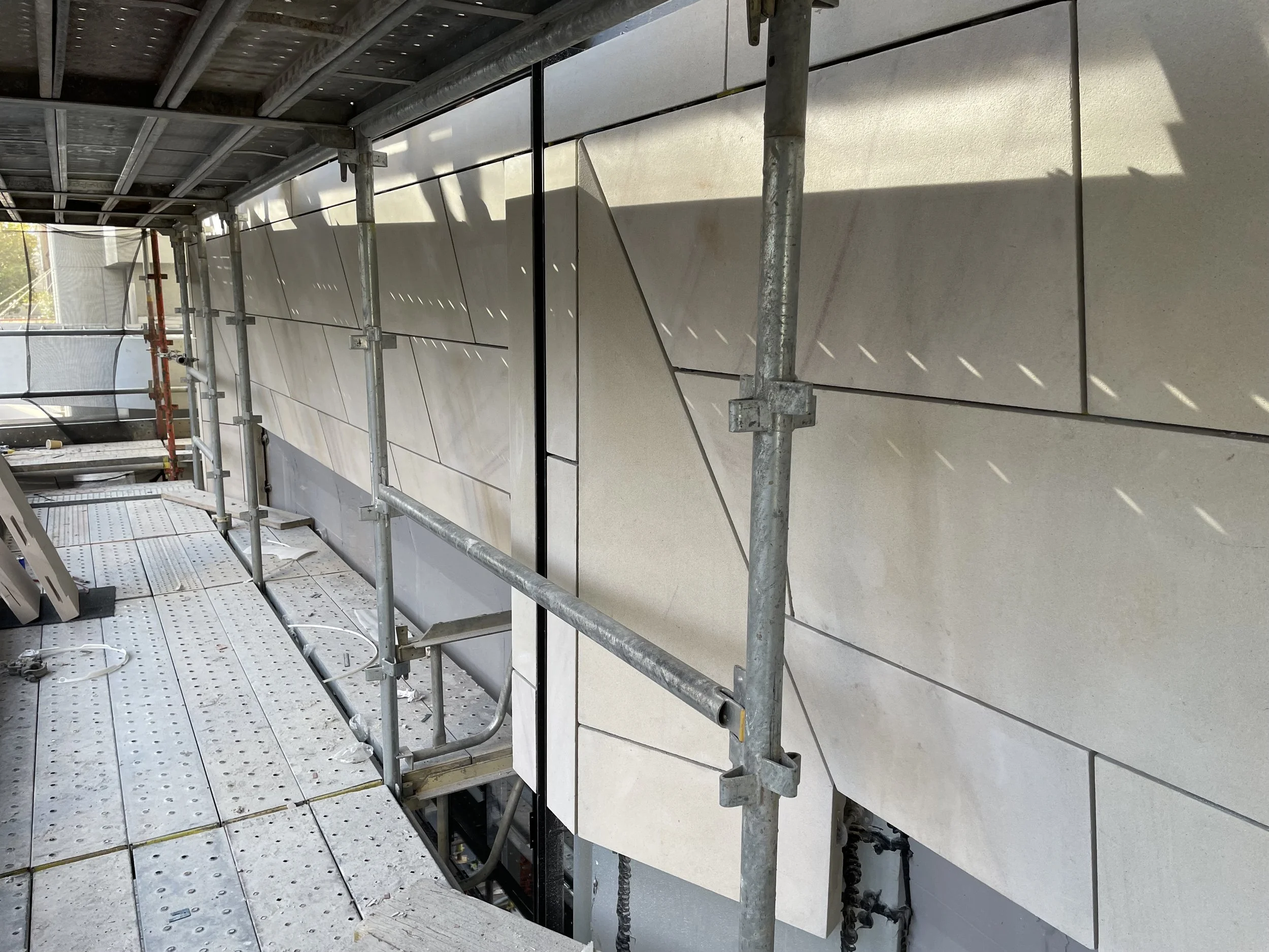 Construction scaffolding and beige tiles on the exterior wall of a building under renovation.