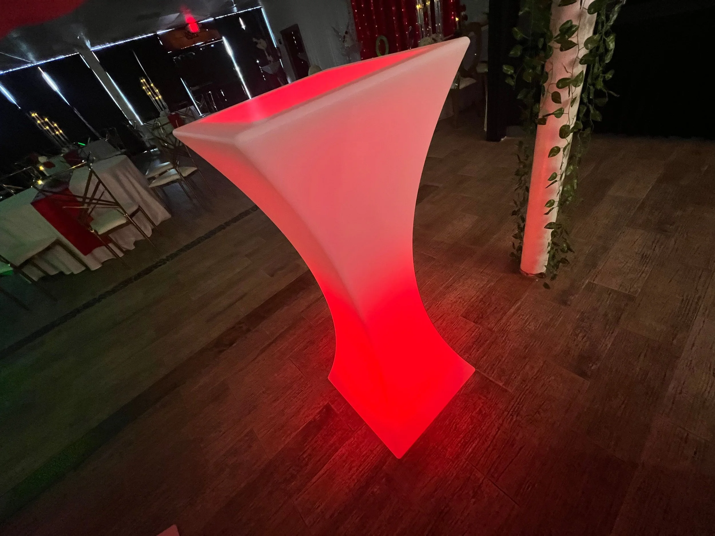 A glowing red and white cocktail table with a sleek, curved design in a dimly lit event space.