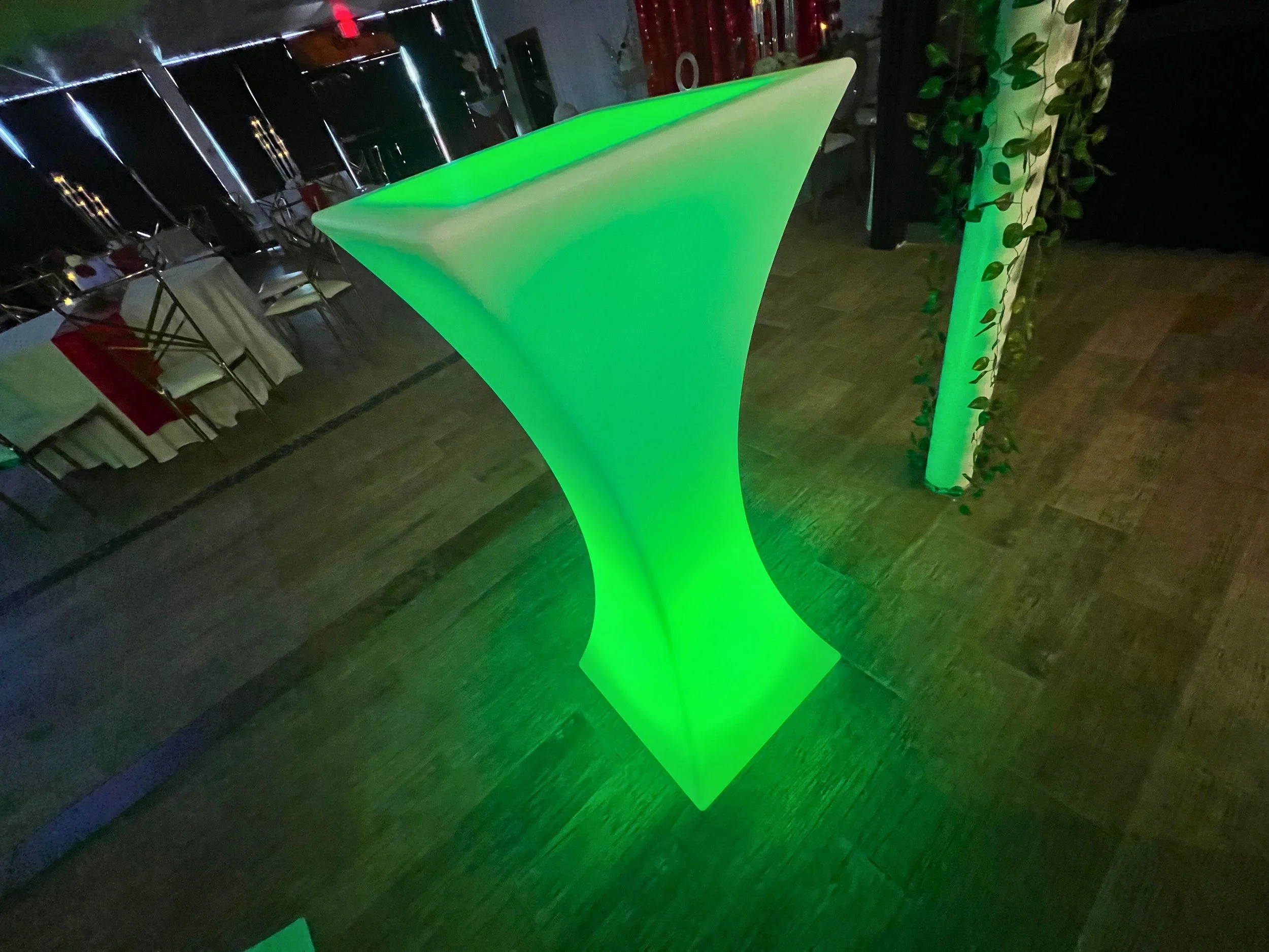 A glowing green modern cocktail or high table in a dimly lit party or event setting.