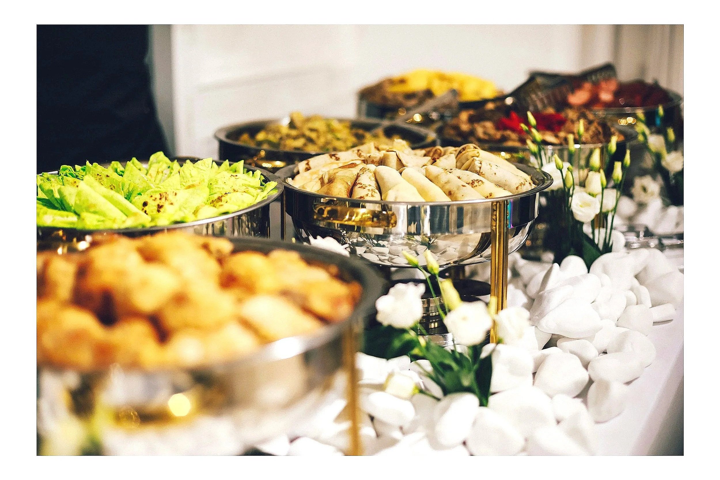 A decorative buffet table displaying assorted wraps, salads, pastas, meats, and vegetables.