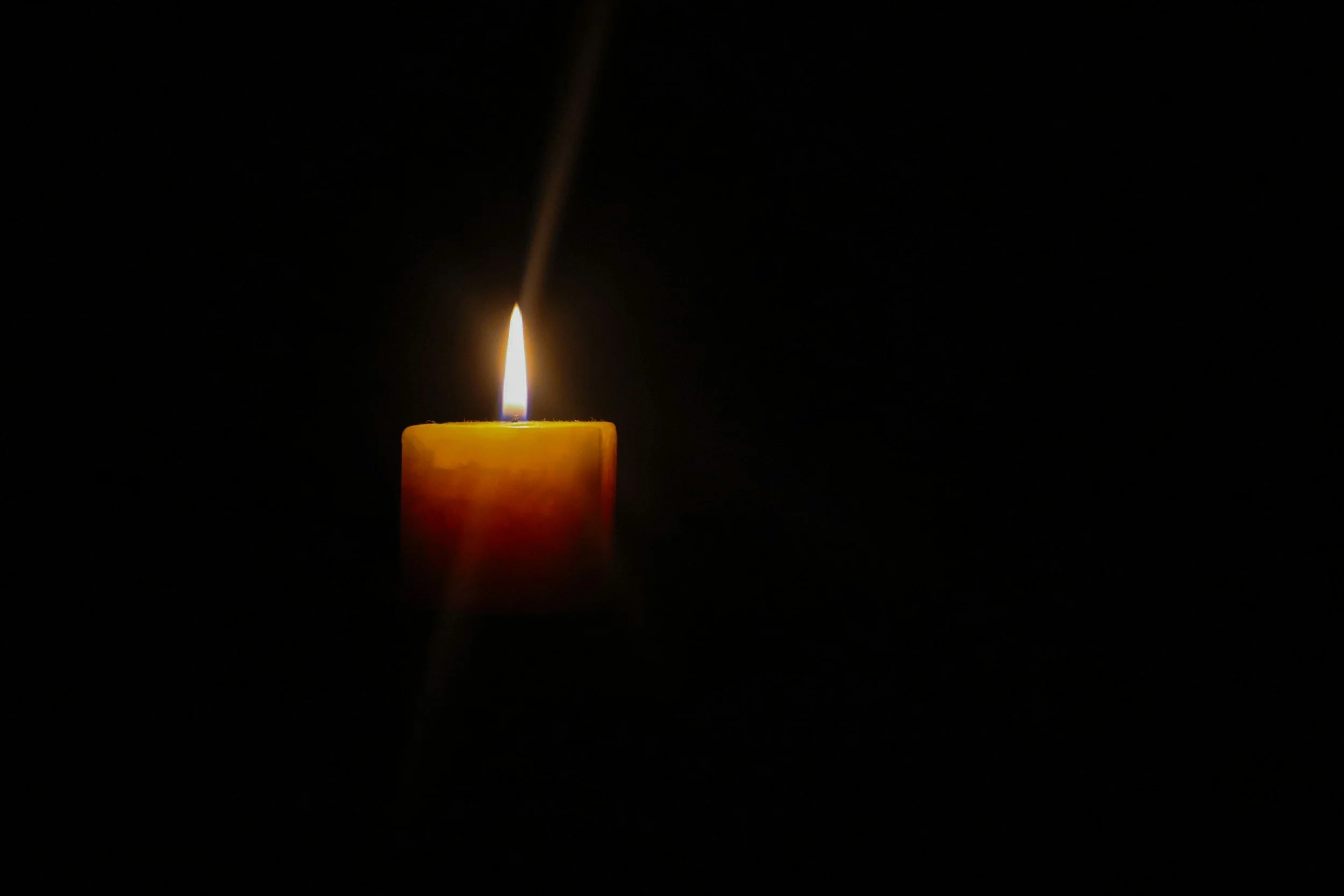 A single lit candle with a flame, set against a dark background.