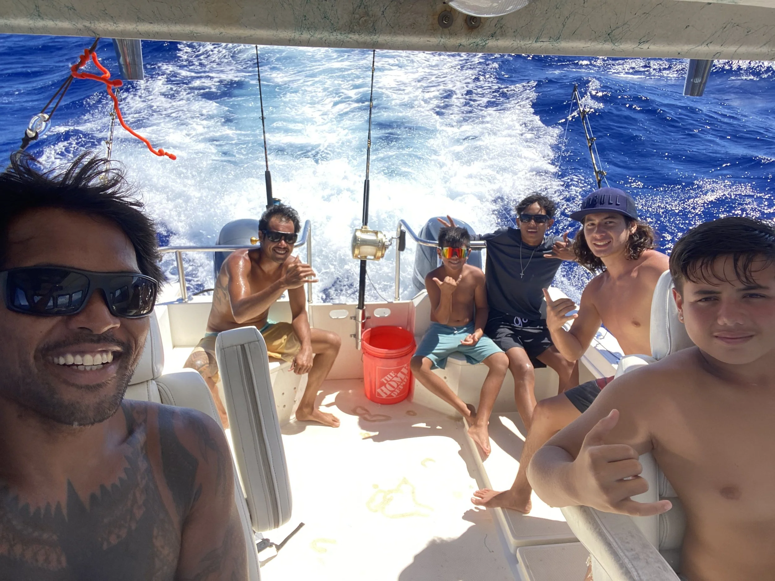 Group of friends enjoying a sunny day on a Kaua‘i boat tour, relaxing on deck with ocean views and splashing water behind them.