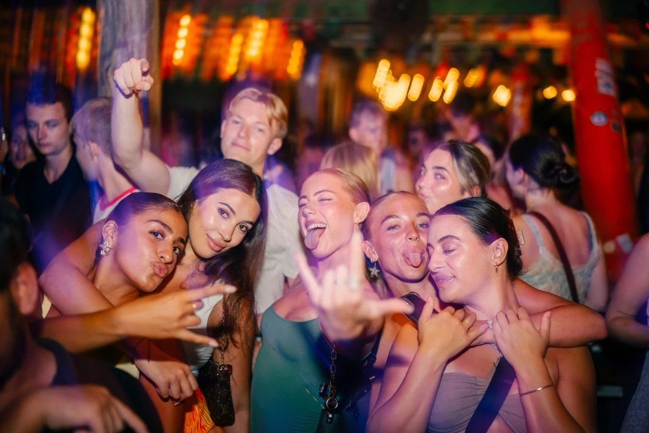 Group of young adults dancing and having fun at a lively party or nightclub with colorful lights.