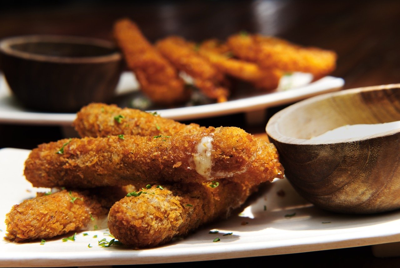 Fried chicken drumsticks on a white plate with dipping sauce and a side of fried chicken wings in the background