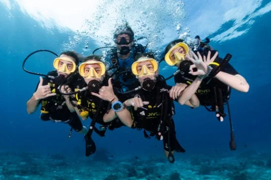 Group of four scuba divers underwater posing for the camera with hand signals.