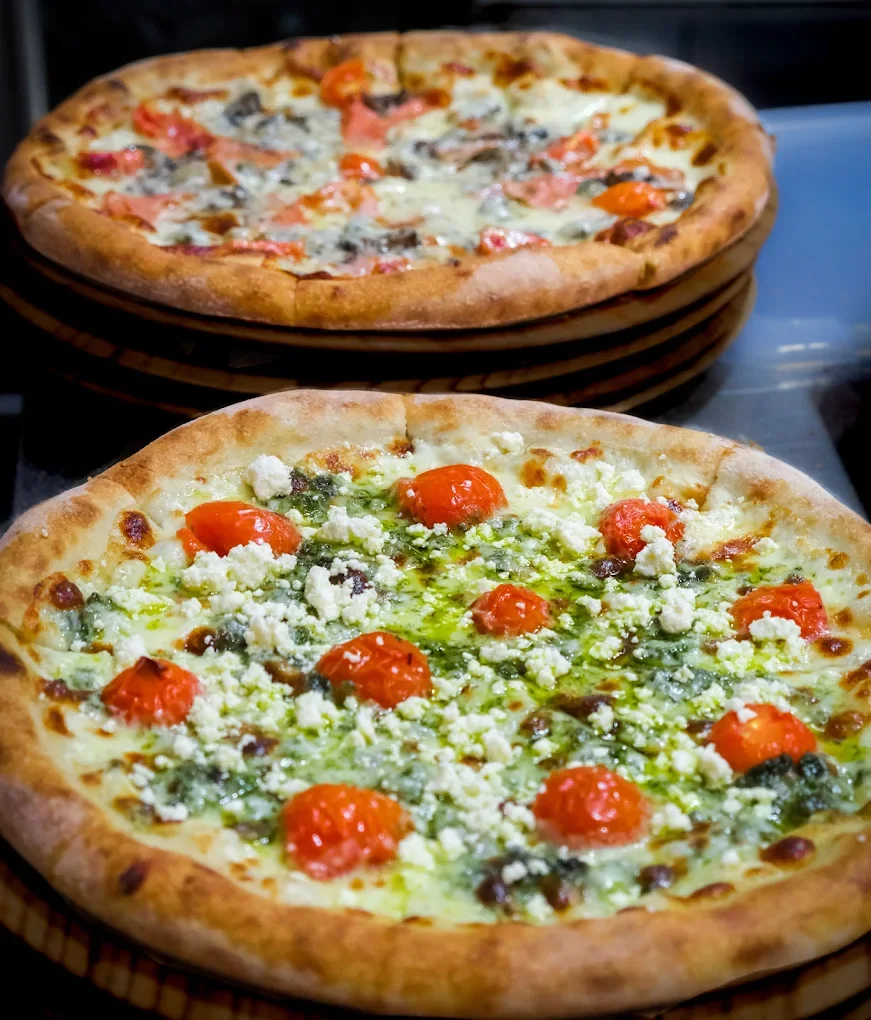 Two pizzas, one with cherry tomatoes, green herbs, and cheese, and another with mushrooms, tomato slices, and cheese, on wooden serving boards.