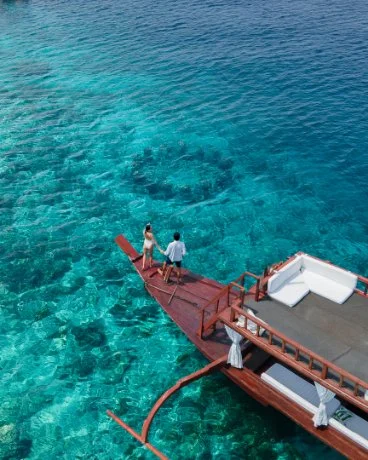 People standing on a wooden dock extending into clear blue ocean water with a submerged submarine visible beneath surface.