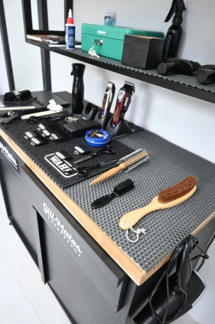 Workstation with various grooming tools, including clippers, brushes, comb, and scissors, on a textured black work surface.
