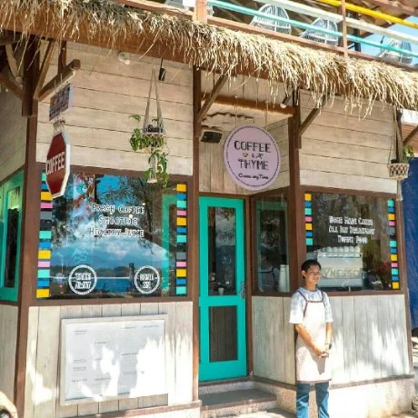 Exterior of a rustic coffee shop with colorful striped accents, a hanging plant, and a woman standing outside.