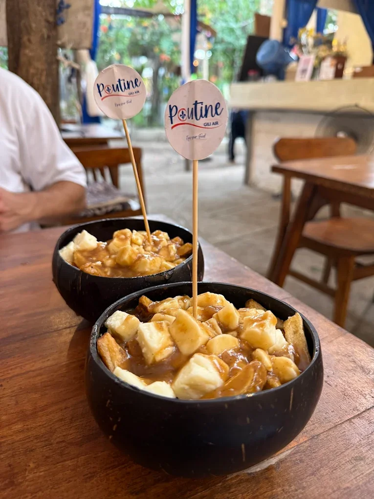 Two black bowls filled with a dessert topped with chunks of bananas, caramel sauce, and other toppings, each with a small flag labeled 'Poutine' on a wooden stick.