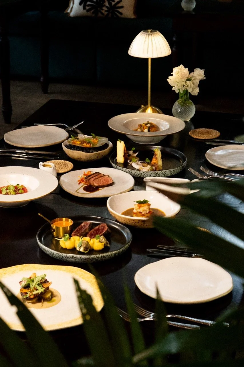 A dining table set with various gourmet dishes, a small table lamp, and a vase with white flowers