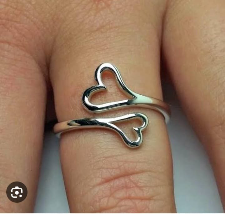 A silver ring with two overlapping heart shapes worn on a finger.