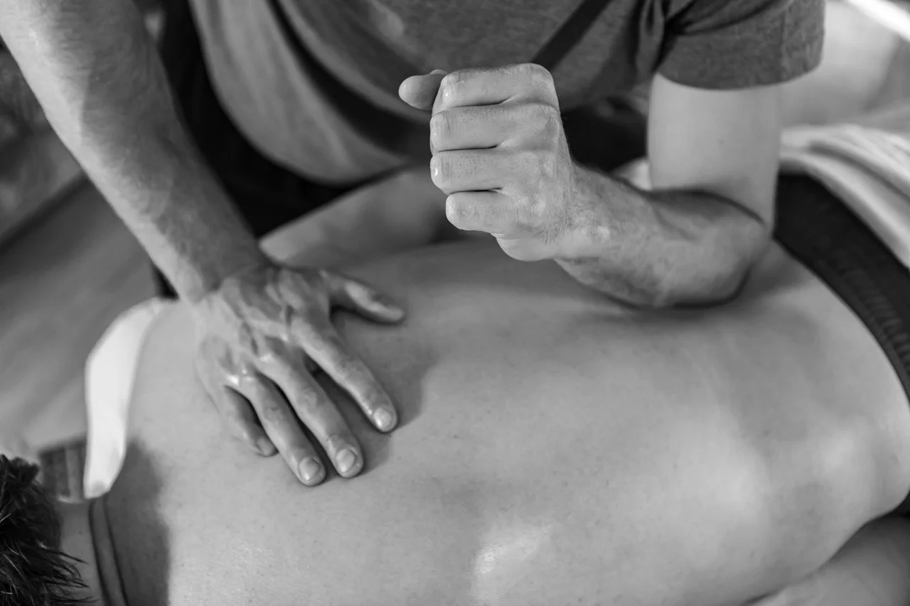 A person receiving a massage, lying face down on a massage table while a massage therapist uses their hands to apply pressure on the person's back.