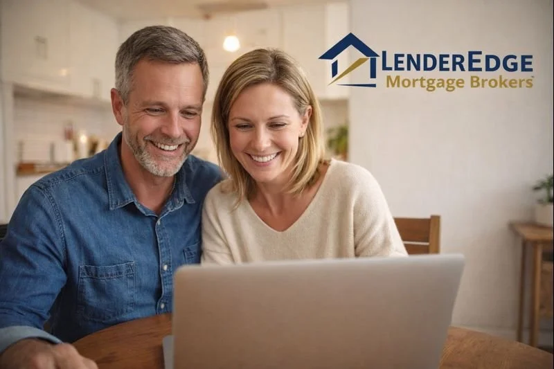 A smiling middle-aged man and woman looking at a laptop screen together at a wooden table in a bright kitchen. The logo for 'LenderEdge Mortgage Brokers' is visible in the top right corner.