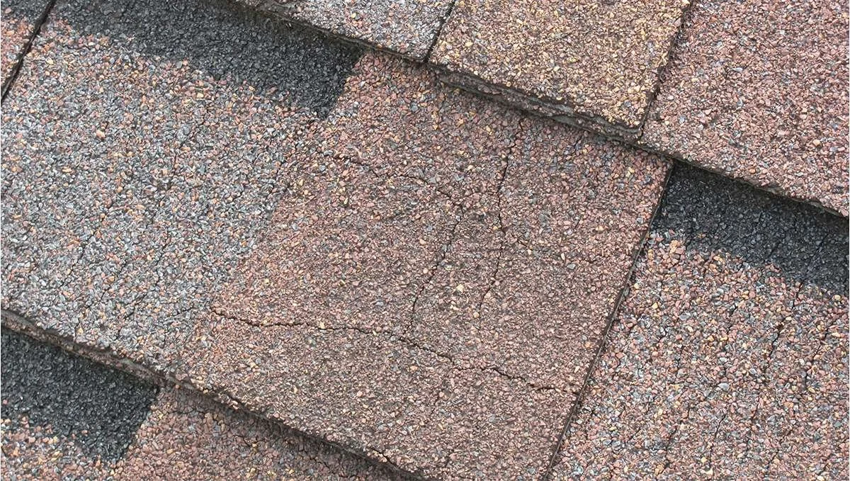 Close-up of a section of asphalt shingles with visible cracks.