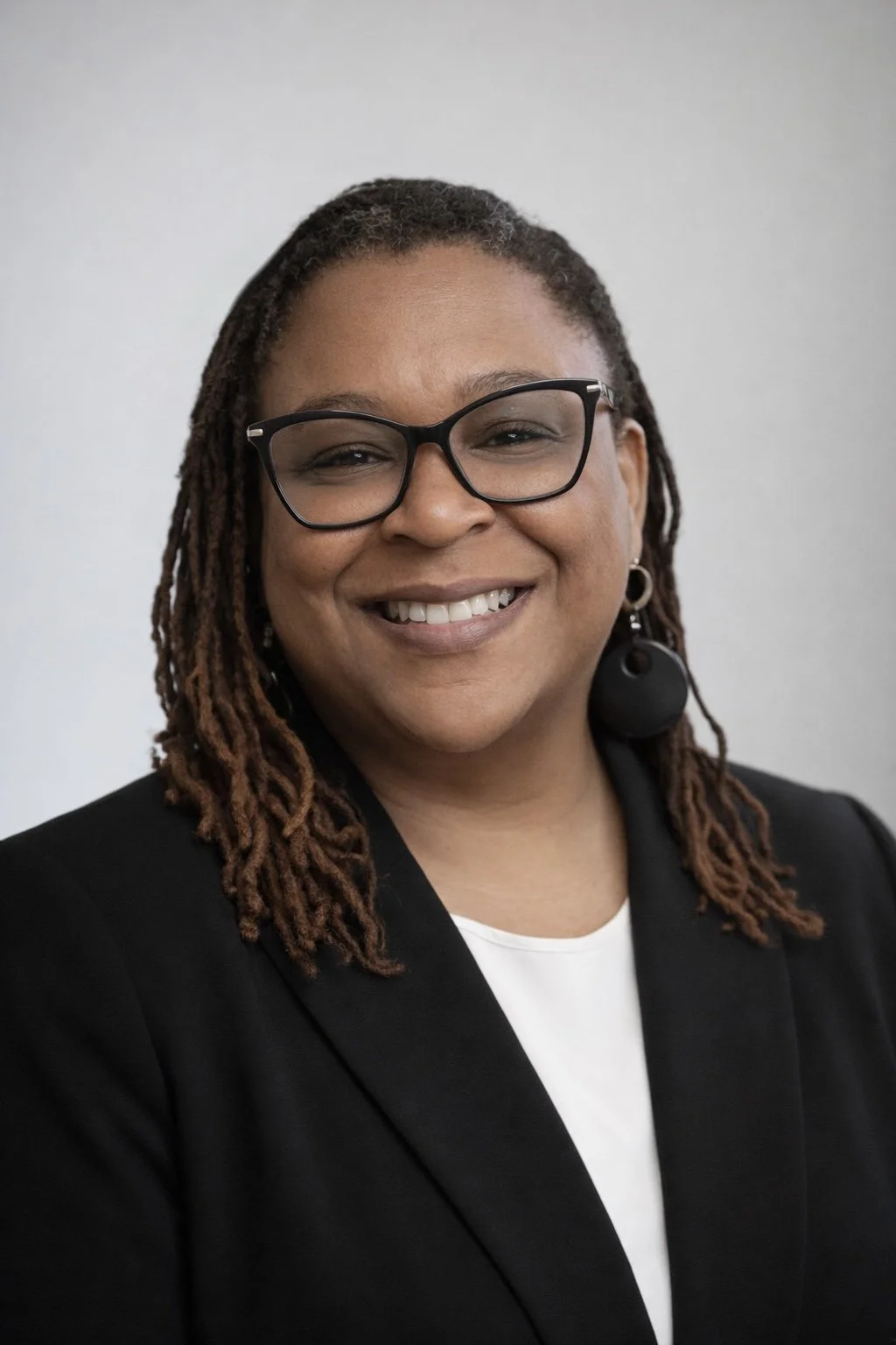 Portrait of owner partner Adriane Barnes, smiling in a black blazer and white top.