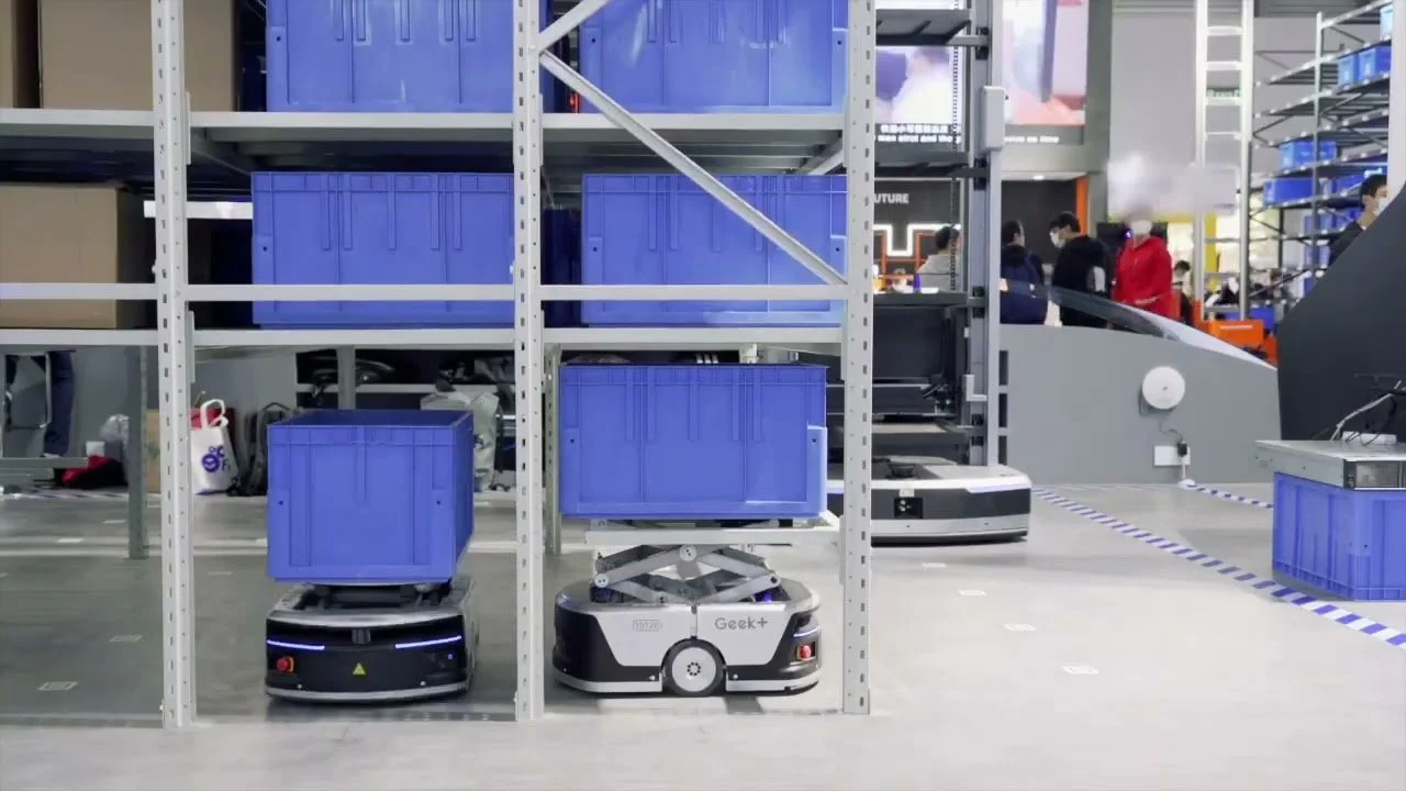 Robots and warehouse shelving with blue storage containers at an exhibition.