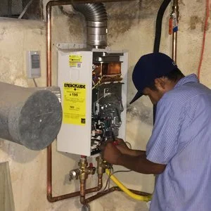 Technician working on a gas furnace or boiler in a basement or utility room with pipes and equipment.