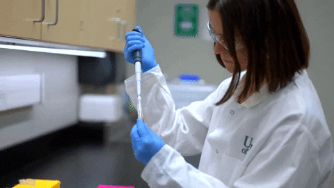 A scientist in a lab coat and blue gloves using a pipette in a laboratory setting