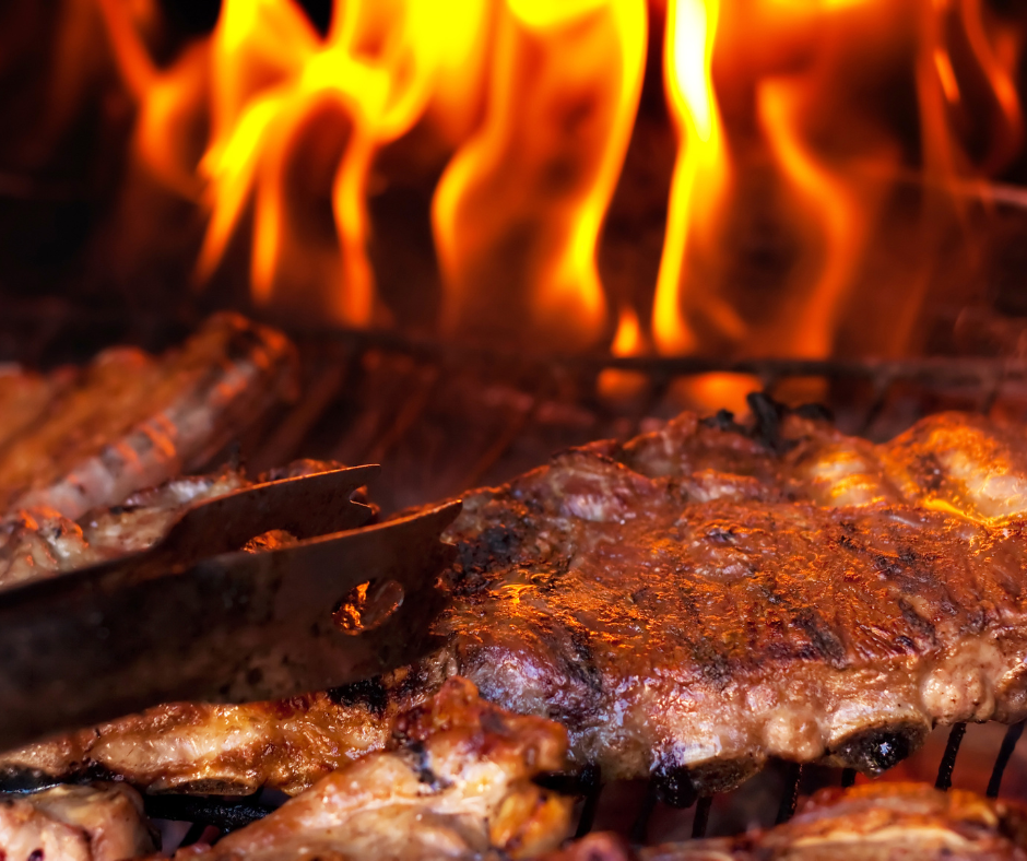 Close-up of meat grilling over open flames, with a spatula flipping the meat.