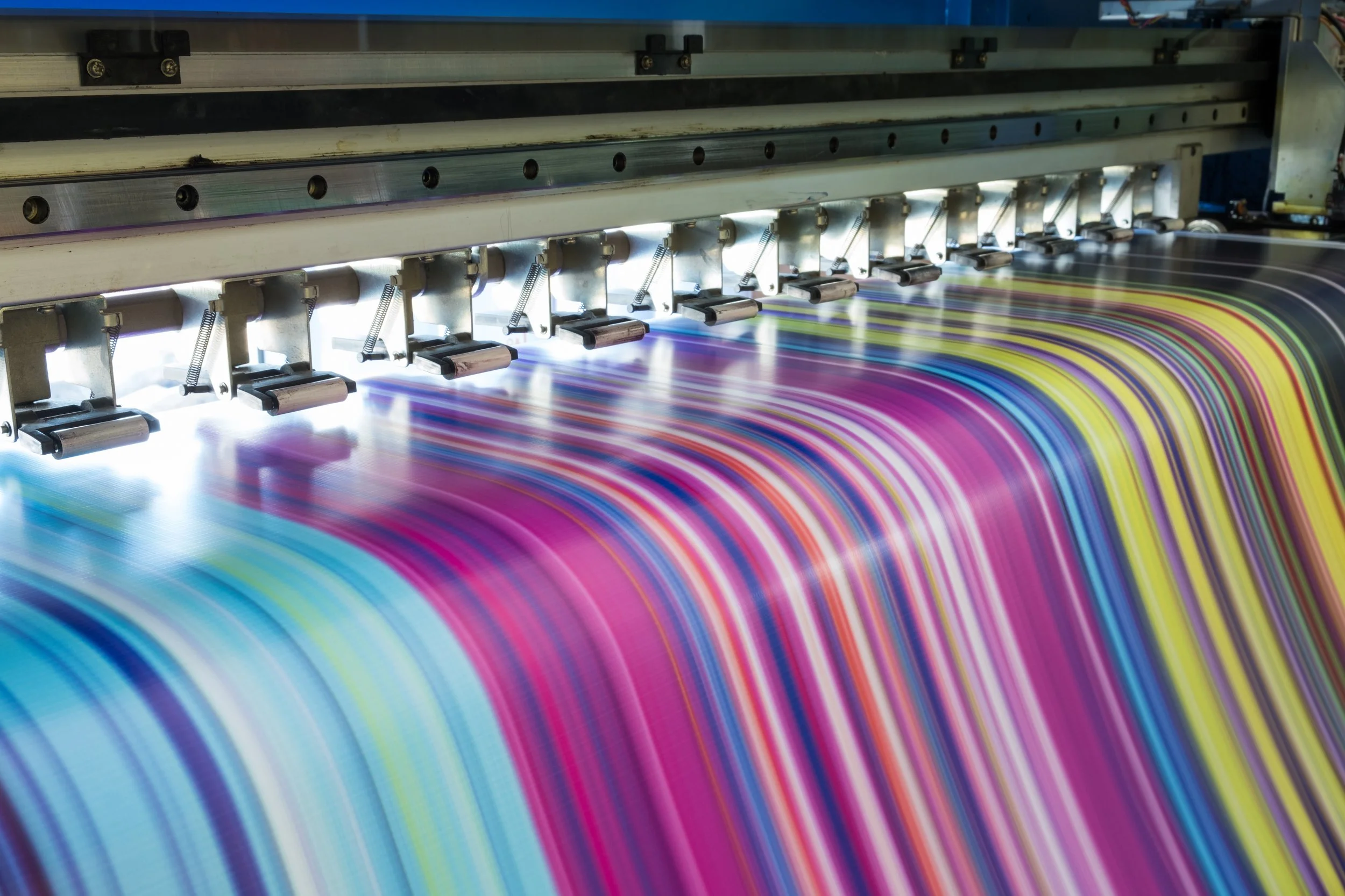 Close-up of a digital printing machine printing colorful, curved lines on paper or fabric.
