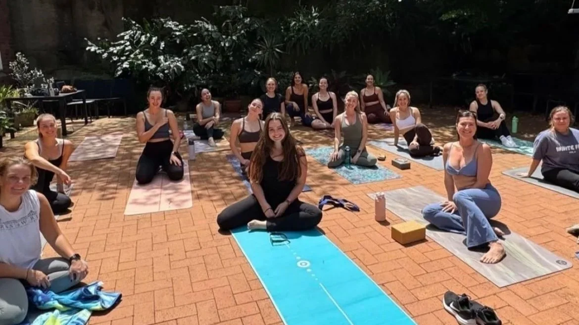 Group of women practising yoga together on an outdoor patio during a private book club wellbeing session in Sydney.