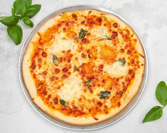 A cheese pizza with some basil leaves on top, served on a round metal tray on a light gray surface, with green leaves on either side.