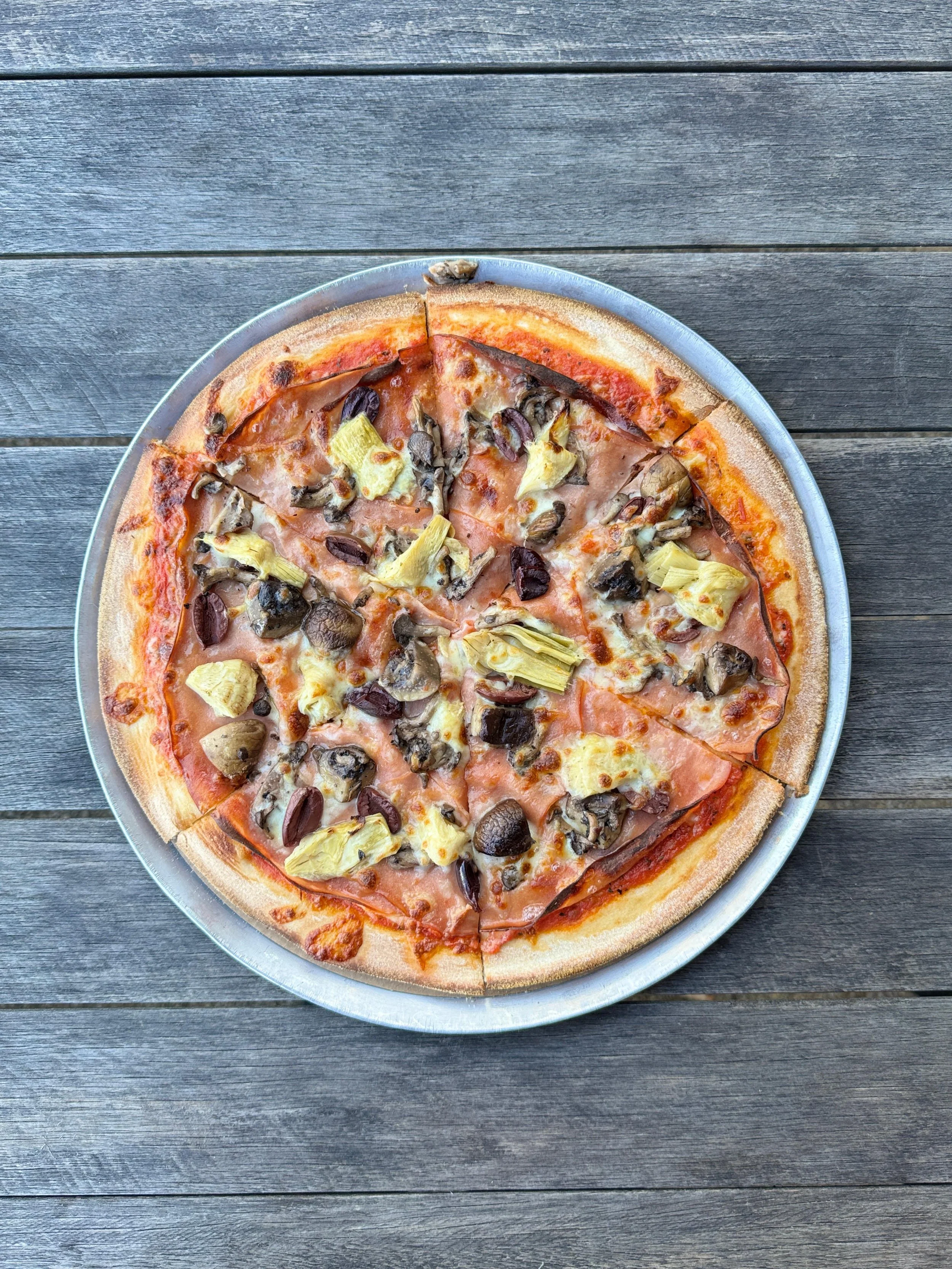 Pizza with mushrooms, artichoke hearts, and black olives on a wooden table.