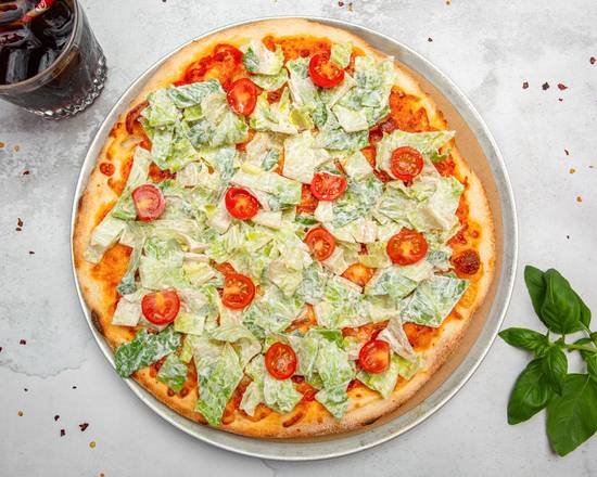 Fresh pizza with lettuce, cherry tomatoes, and cheese on a plate with a glass of soda and basil leaves nearby.