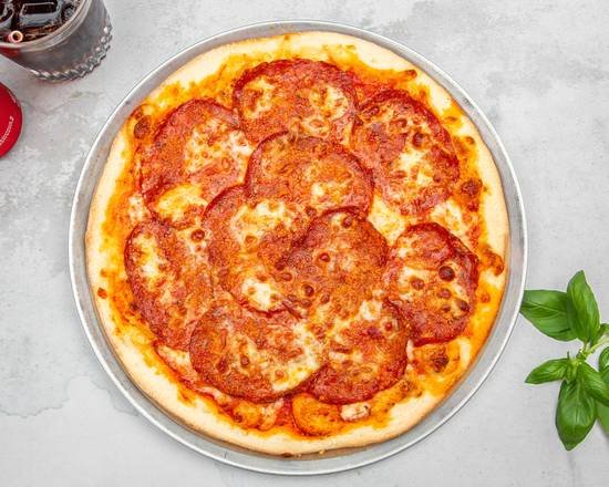 Pepperoni pizza on a metal tray with a glass of soda and a basil plant nearby.