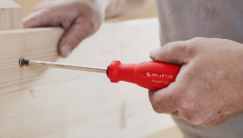 Person using a red-handled screwdriver to screw a wood piece.