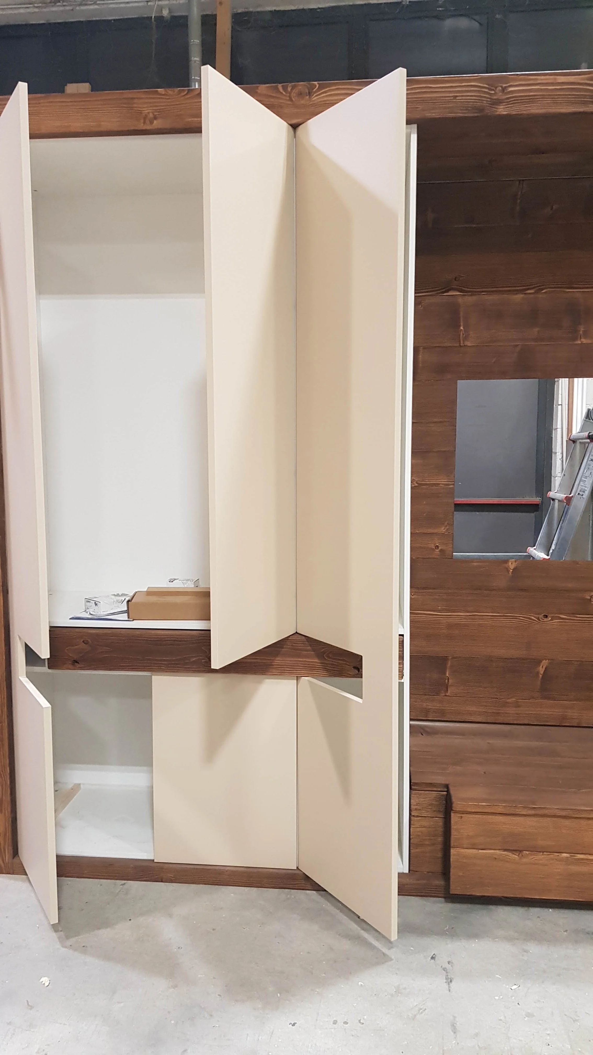 Armadio bianco con ante a battente in fase di installazione, posizionato davanti a una parete di legno.
