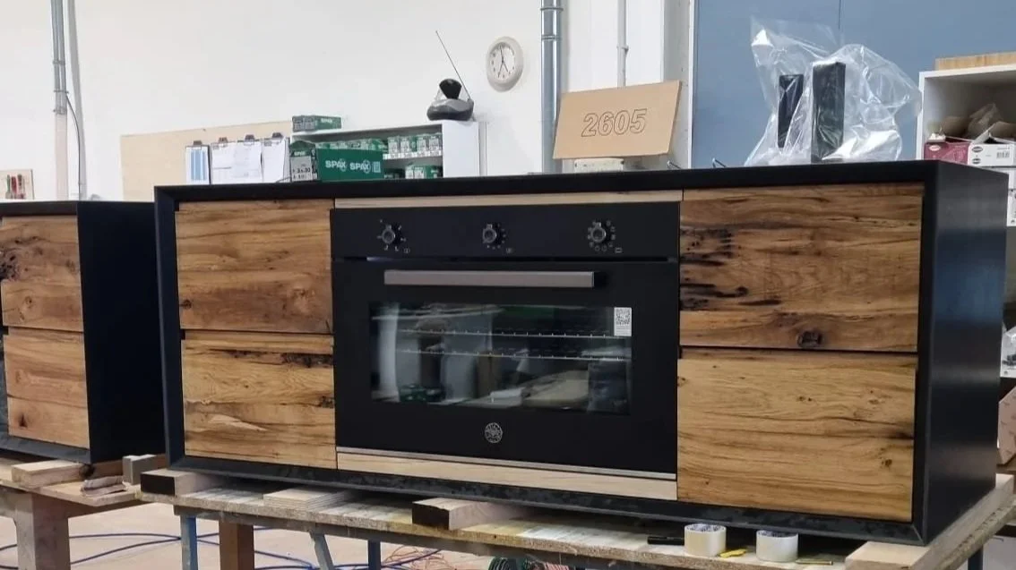 Una cucina moderna con elettrodomestici integrati, tra cui un forno nero incassato in una struttura di legno naturale e acciaio.