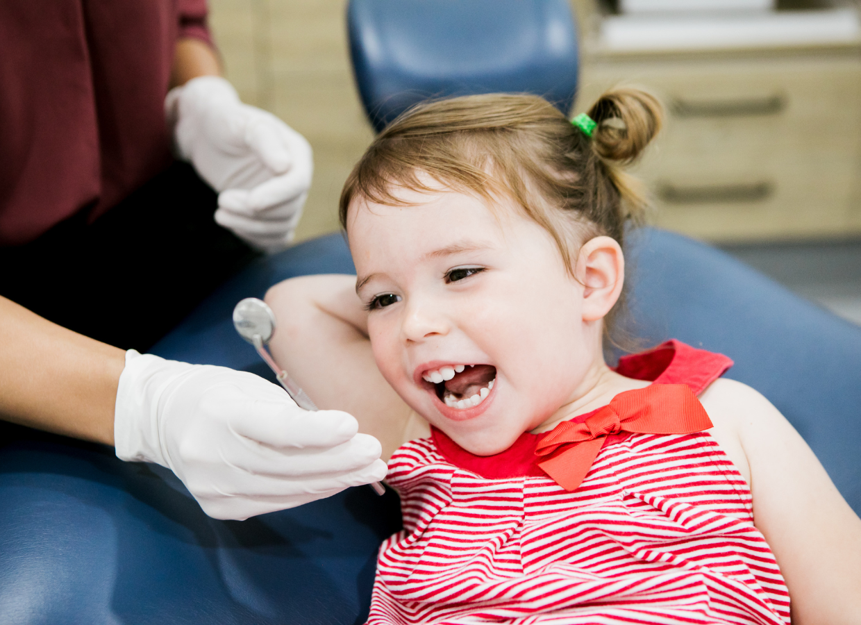 Young girl in a red and white striped dress receiving a dental checkup with the dentist using a mirror.