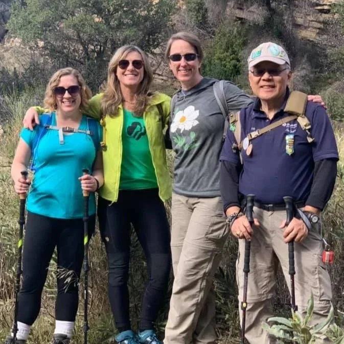 Four Girl Scout leaders standing on trail with packs and hiking poles.