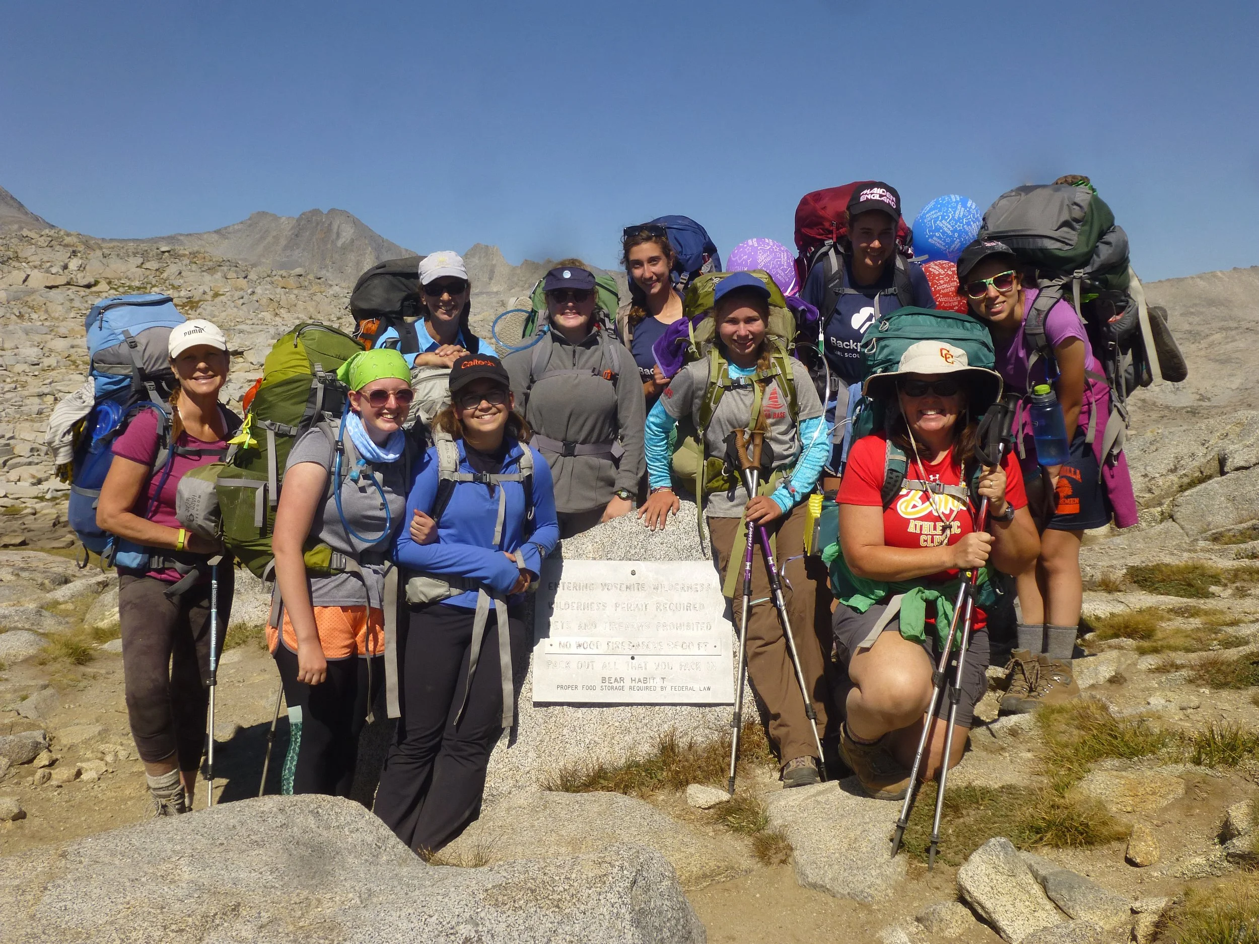 A group of 10 Girl Scout Backpackers at the top of a rocky summit surrounding a summit marker.