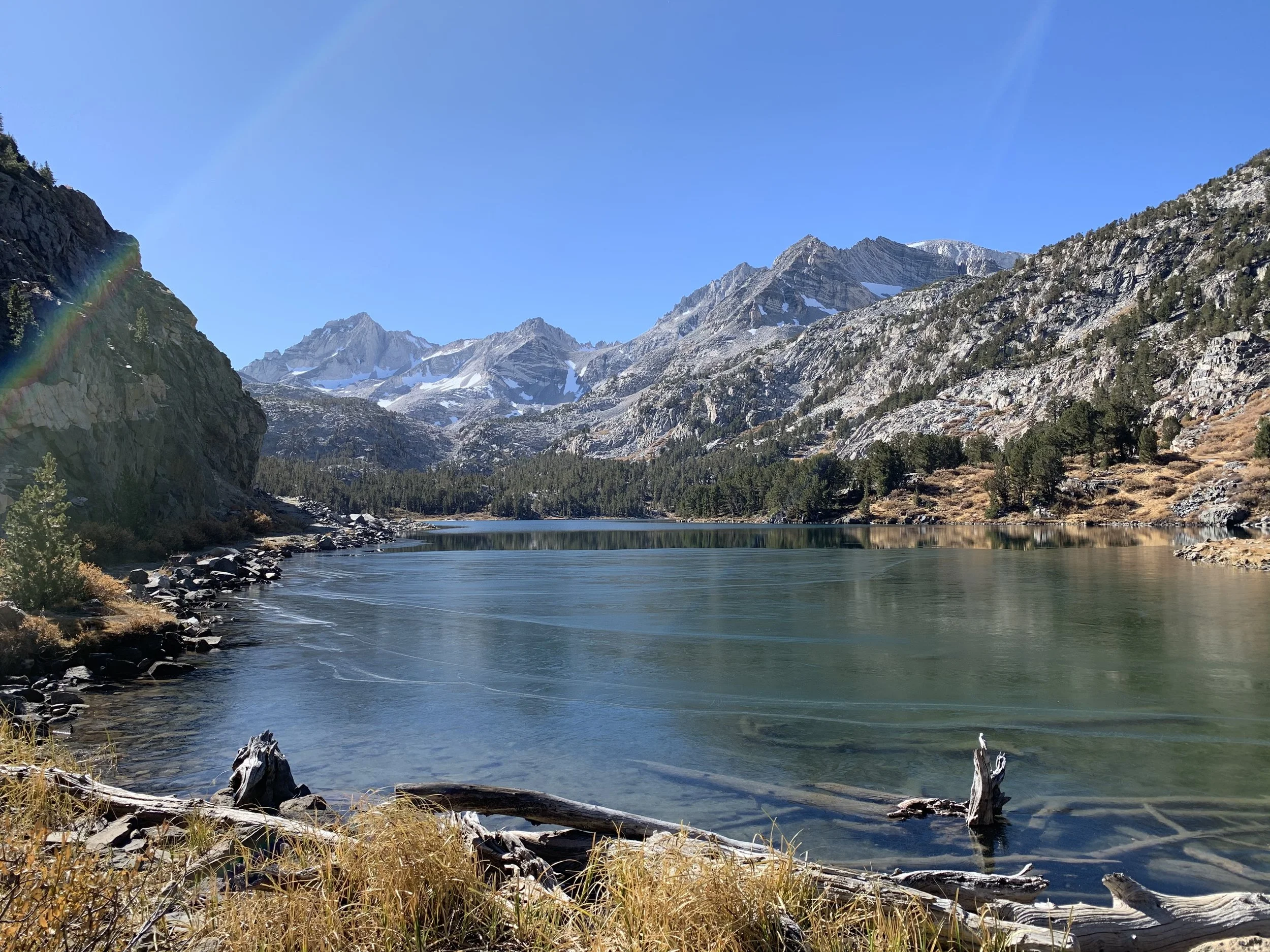 A beautiful, deep blue, alpine lake surrounded by large rock hills and snow dotted mountains in the distance.