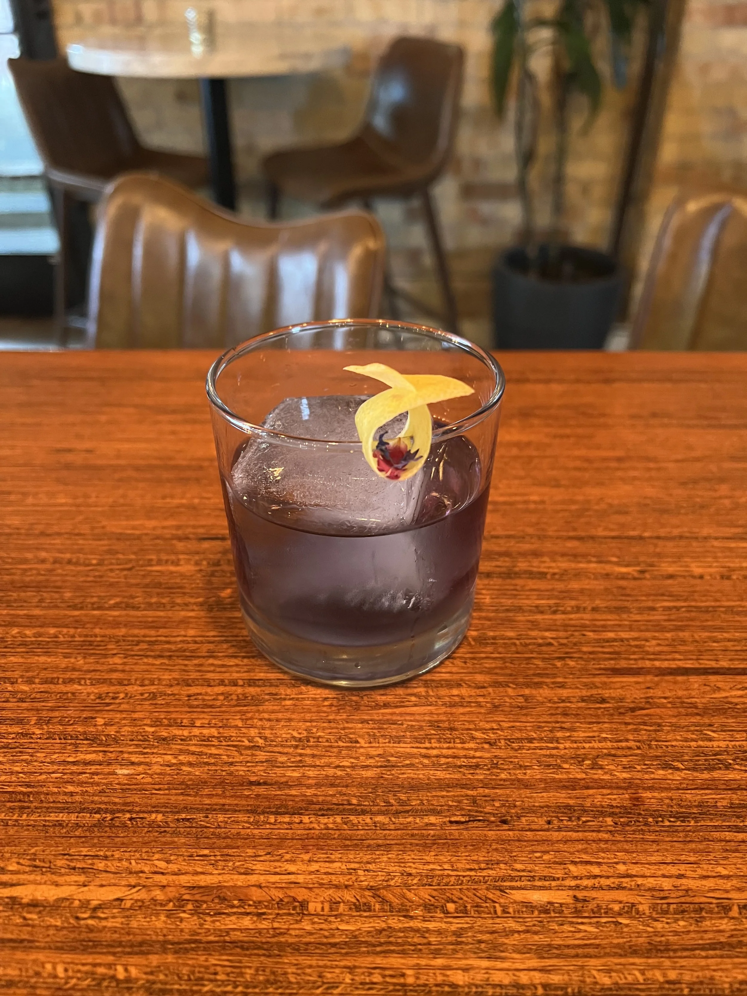 A glass of water with ice and a lemon twist garnish on a wooden table in a restaurant or cafe setting.