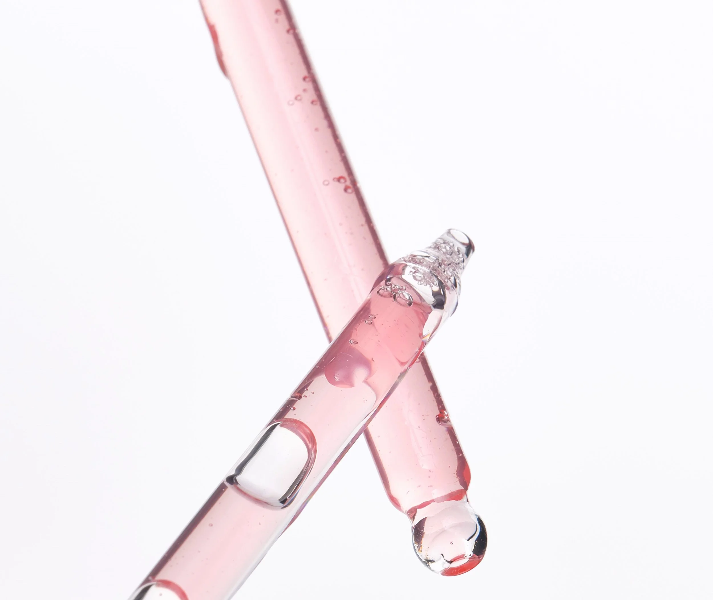 Two glass test tubes with pink liquid and bubbles crossing each other against a white background.