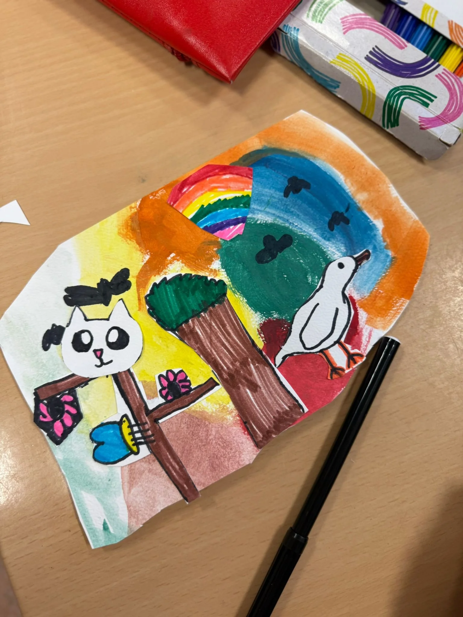 Kindertekening van een regenboog, boom en dieren tijdens creatieve workshop.
