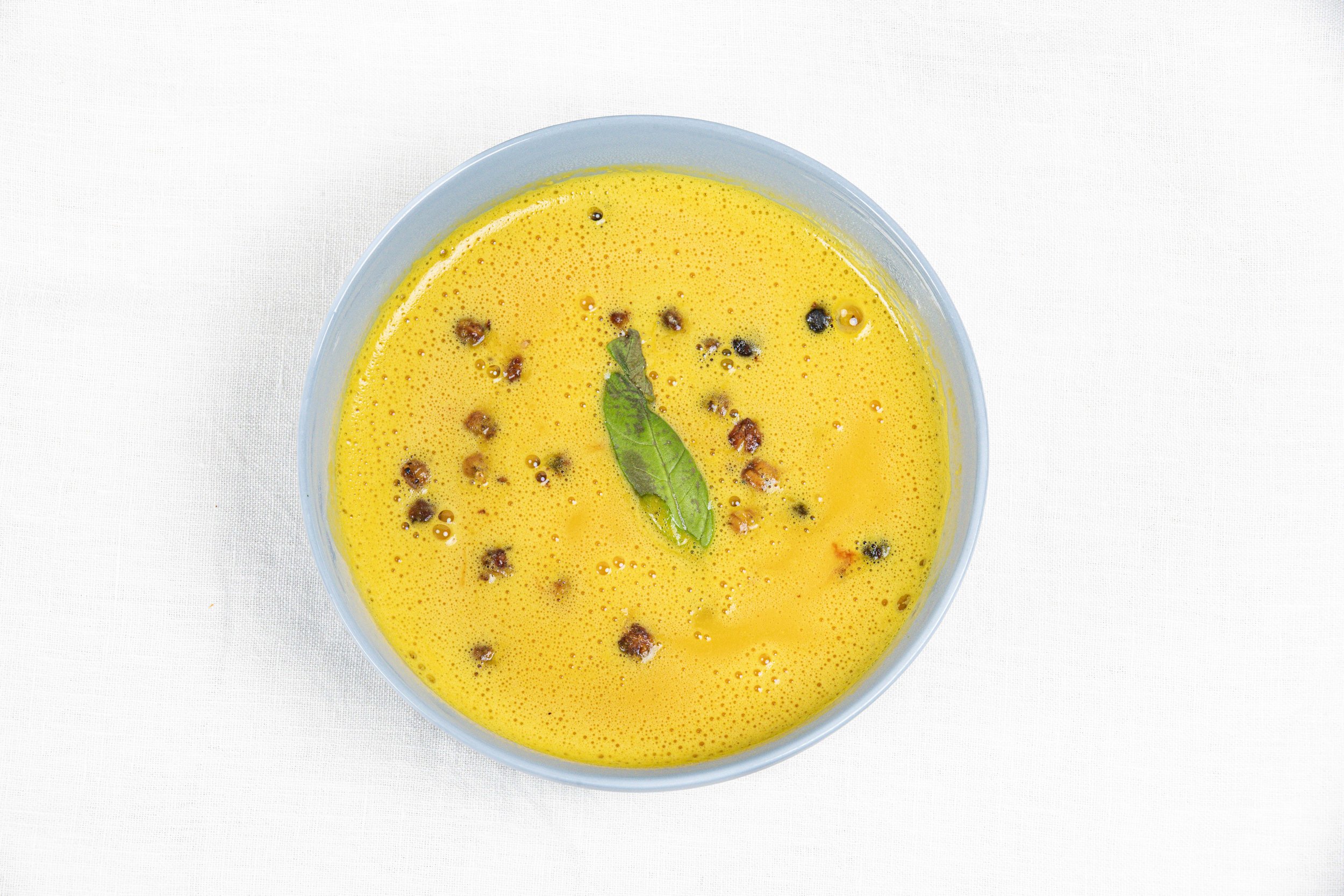 Soupe de curry à la citrouille dans un bol bleu, garnie de feuilles de curry et de graines de moutarde. Par le photographe culinaire Yves Daniel. 