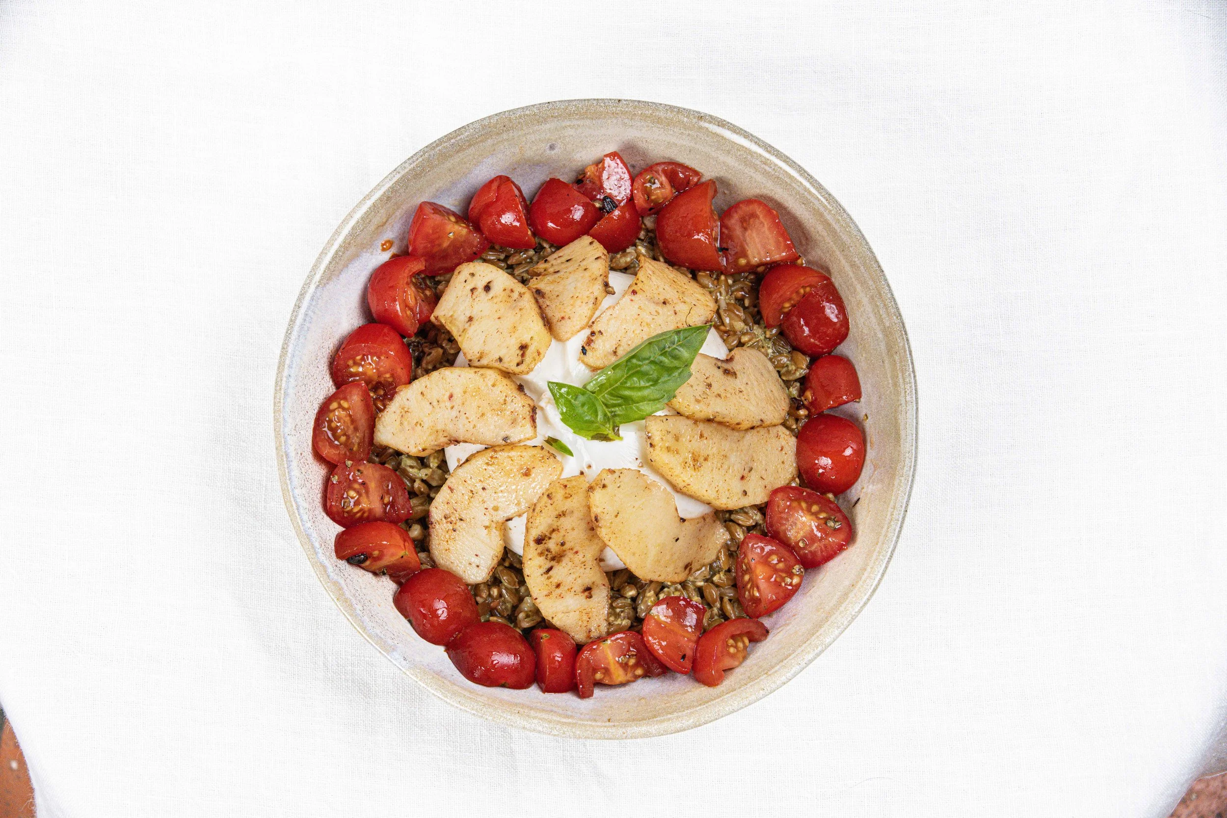 Salade de quinoa avec tomates cerises, morceaux de poulet, basilic, et sauce blanche dans un bol. Par le photographe culinaire Yves Daniel. 